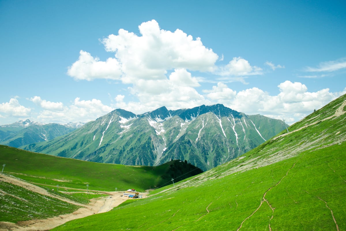 A broad green valley beneath a mountain ridge and billowing white clouds