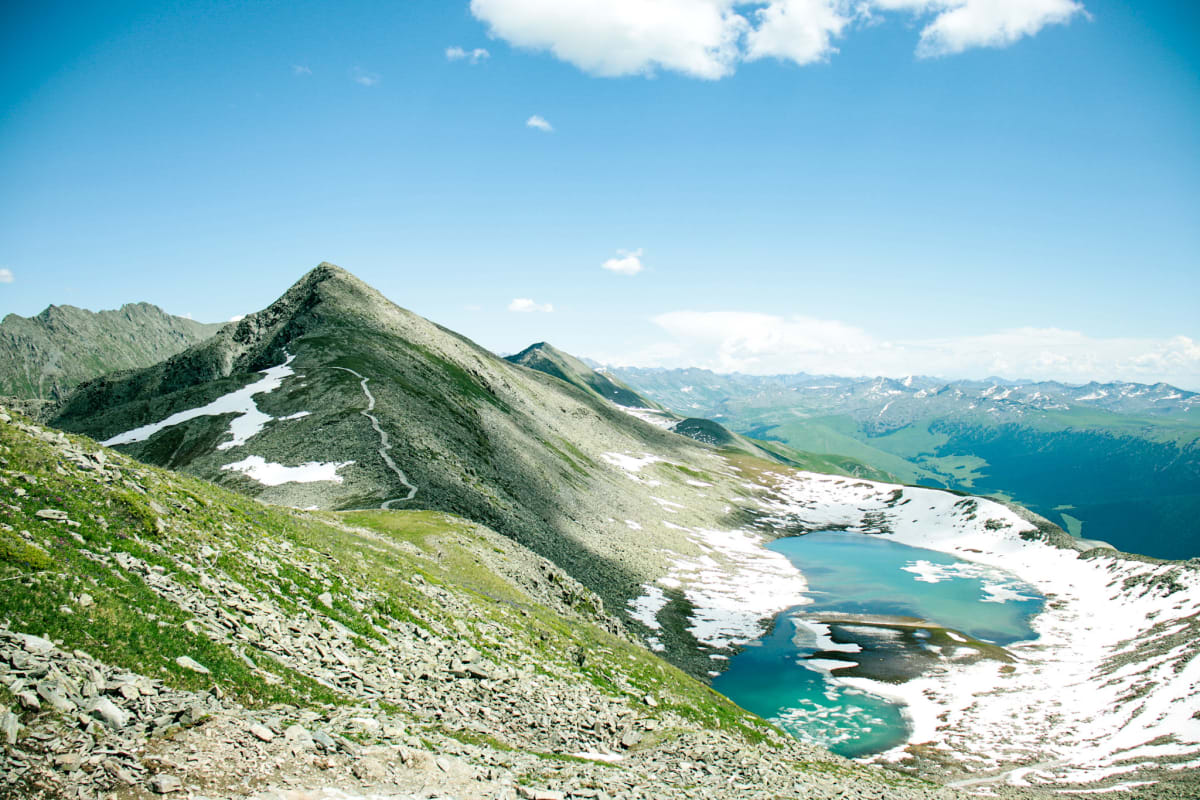 A turquoise alpine lake surrounded by snow-covered mountains beneath a blue sky