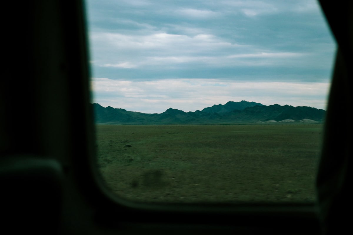 A distant mountain range seen through a vehicle window beneath an overcast sky