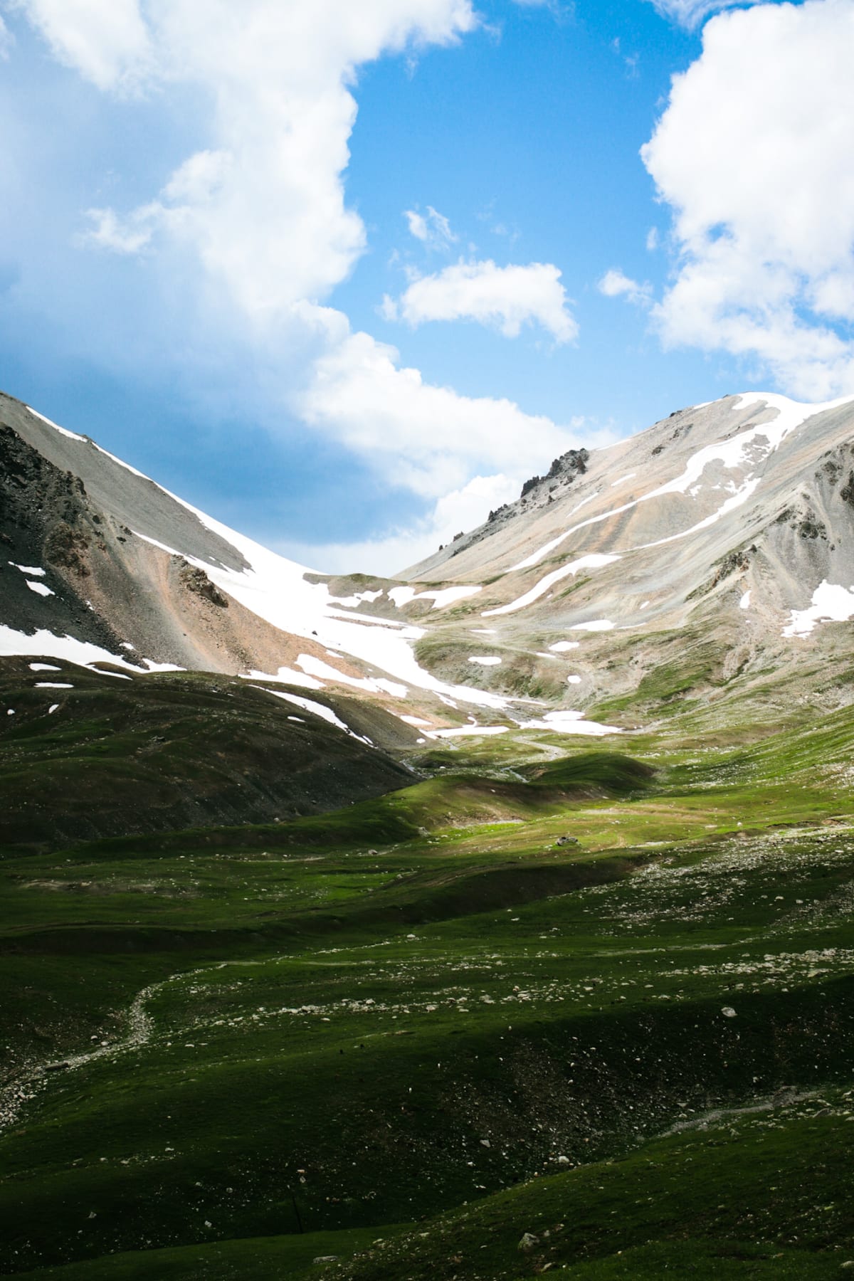 Green slopes and snow-streaked mountains beneath bright clouds