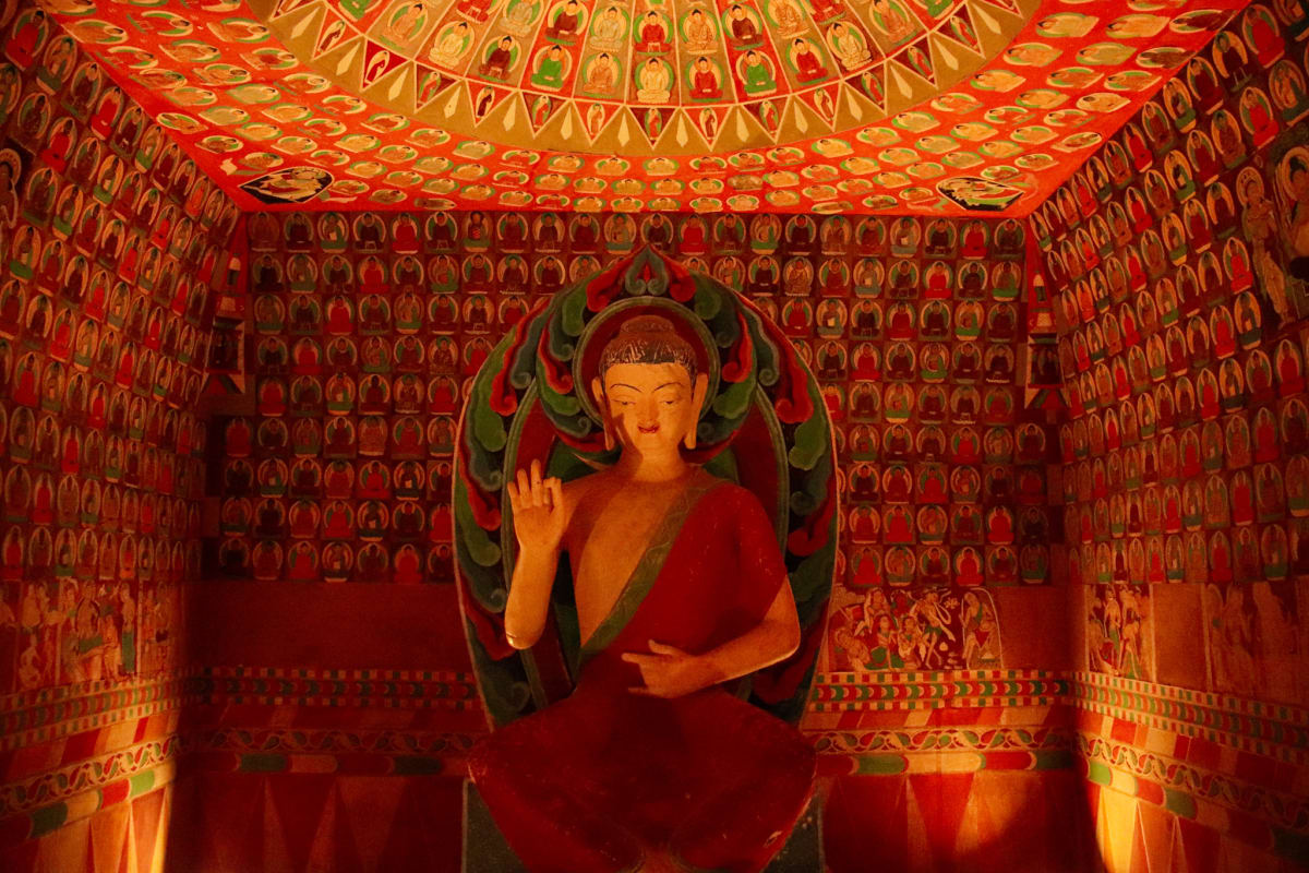 A seated Buddha figure surrounded by rows of painted figures in a red shrine