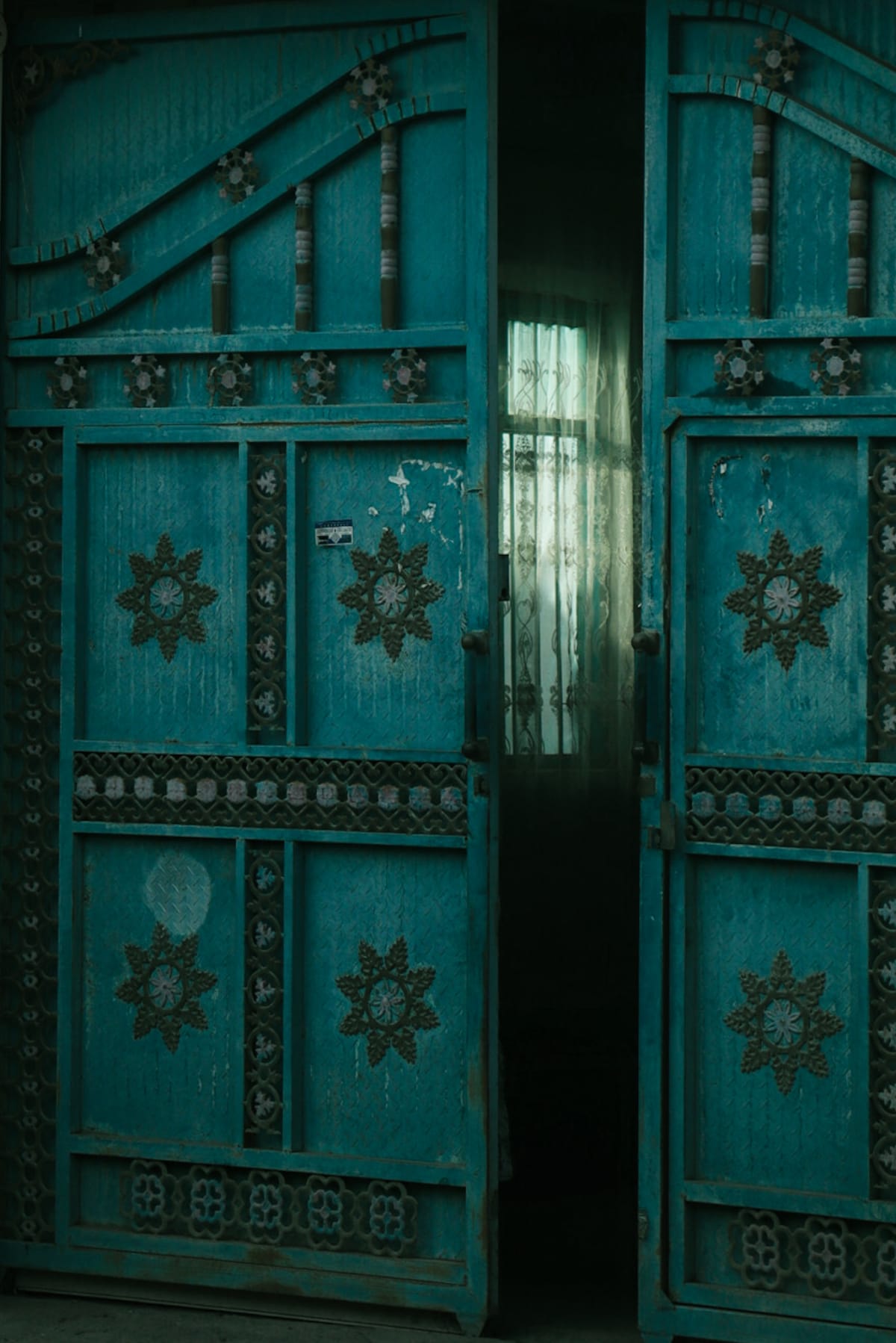 A partially open turquoise door decorated with geometric metalwork