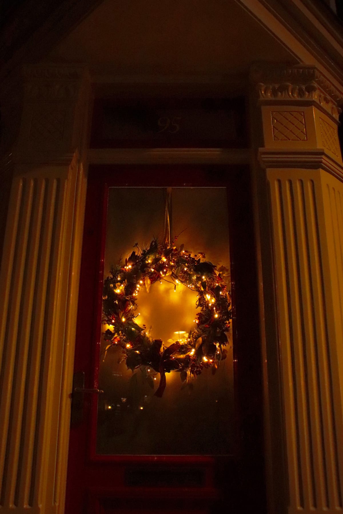 A glowing Christmas wreath hanging on a dark red doorway