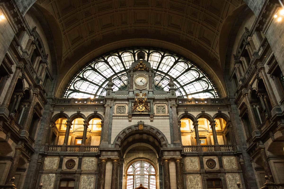 A grand railway station interior with a clock beneath an arched glass roof