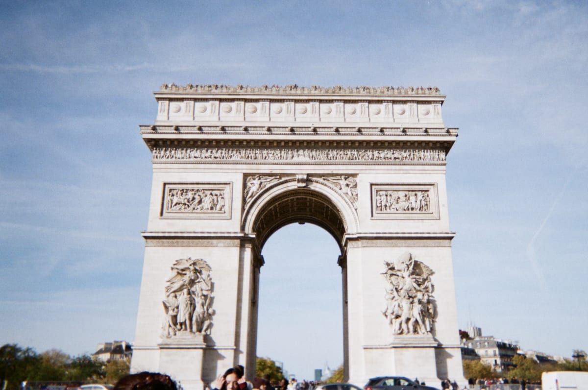 A soft film photograph of the Arc de Triomphe beneath a blue sky