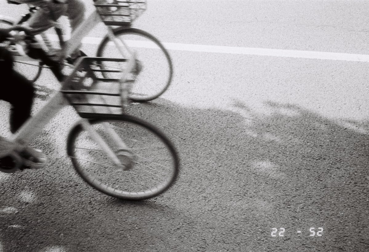 A grainy black-and-white photograph of cyclists moving along a city street