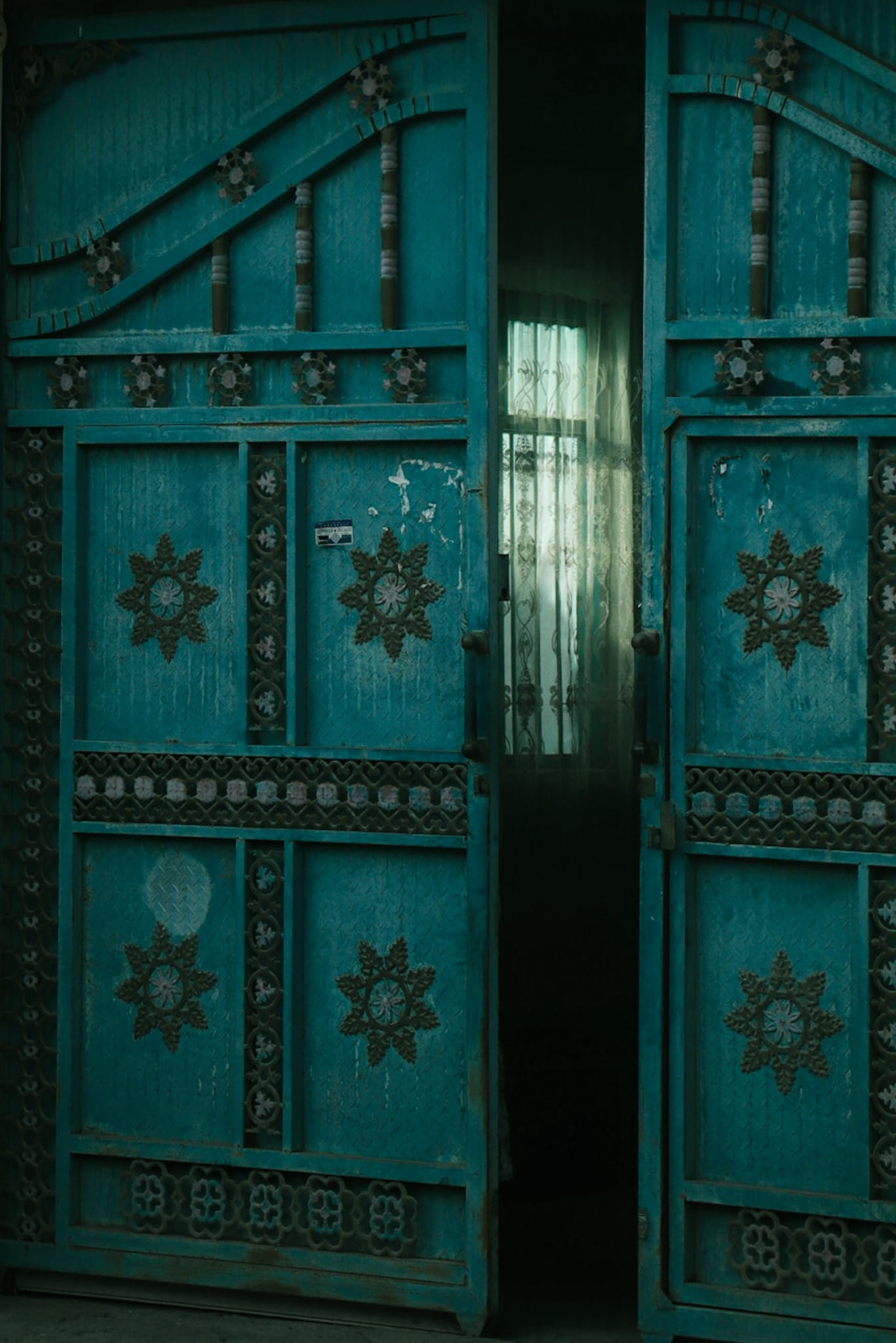 A partially open turquoise door decorated with geometric metalwork