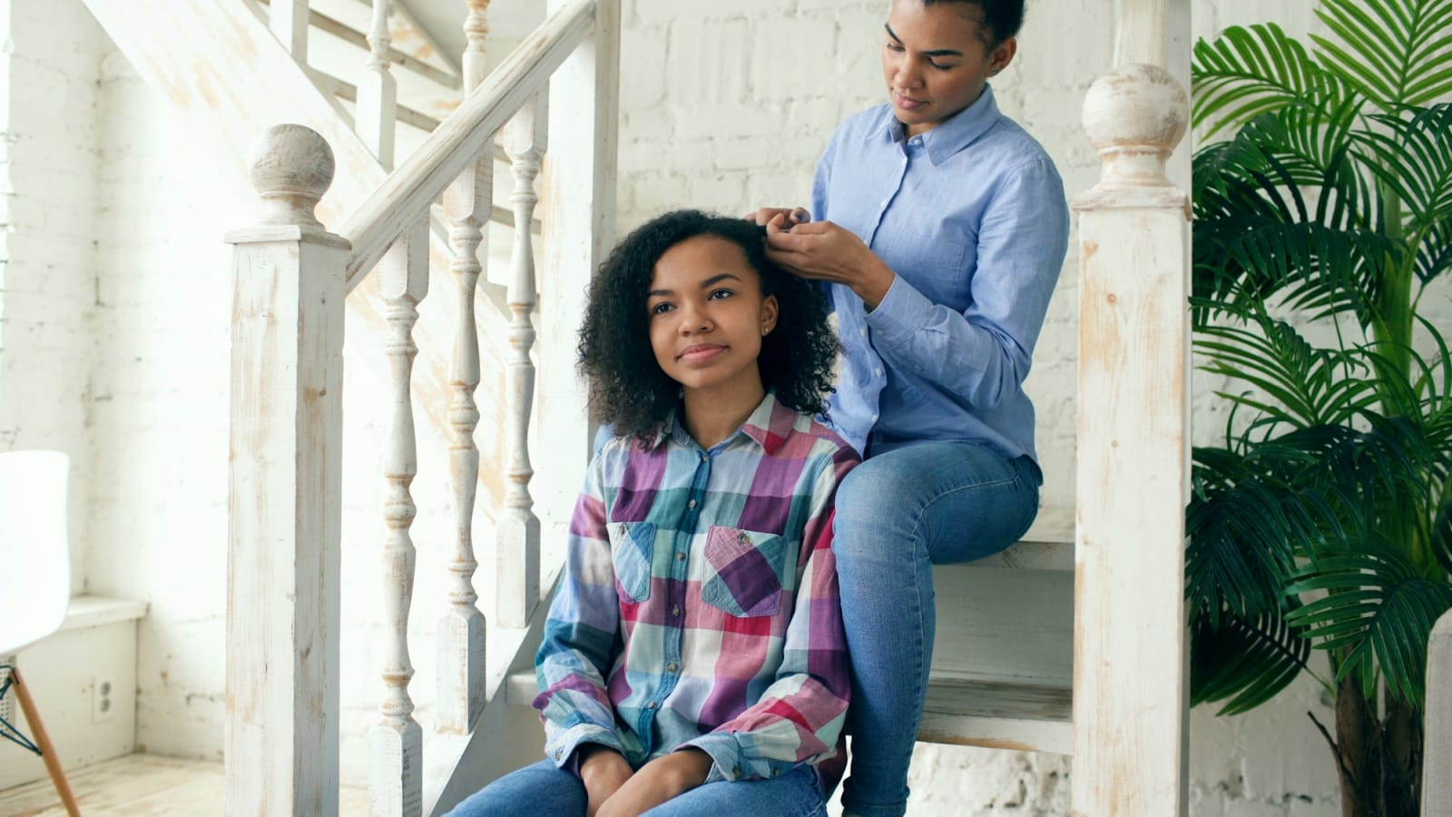 A mother and her teenage daughter sitting together on the stairs at home