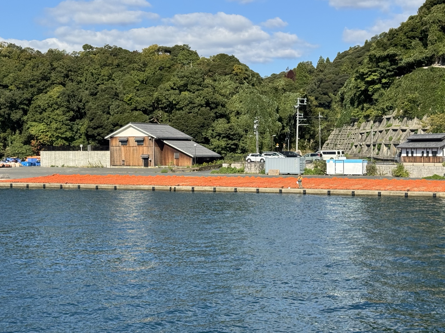 Orange nets along the quay beneath wooded hills