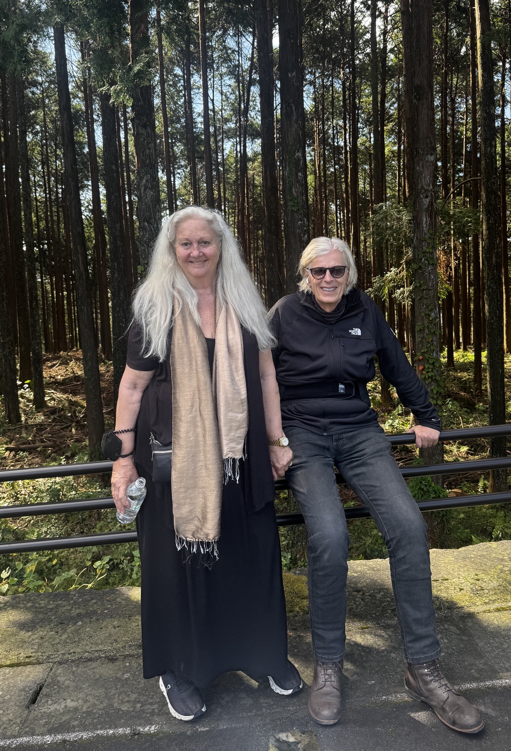 Kurt and Anneliese stand beside a black railing in woodland.