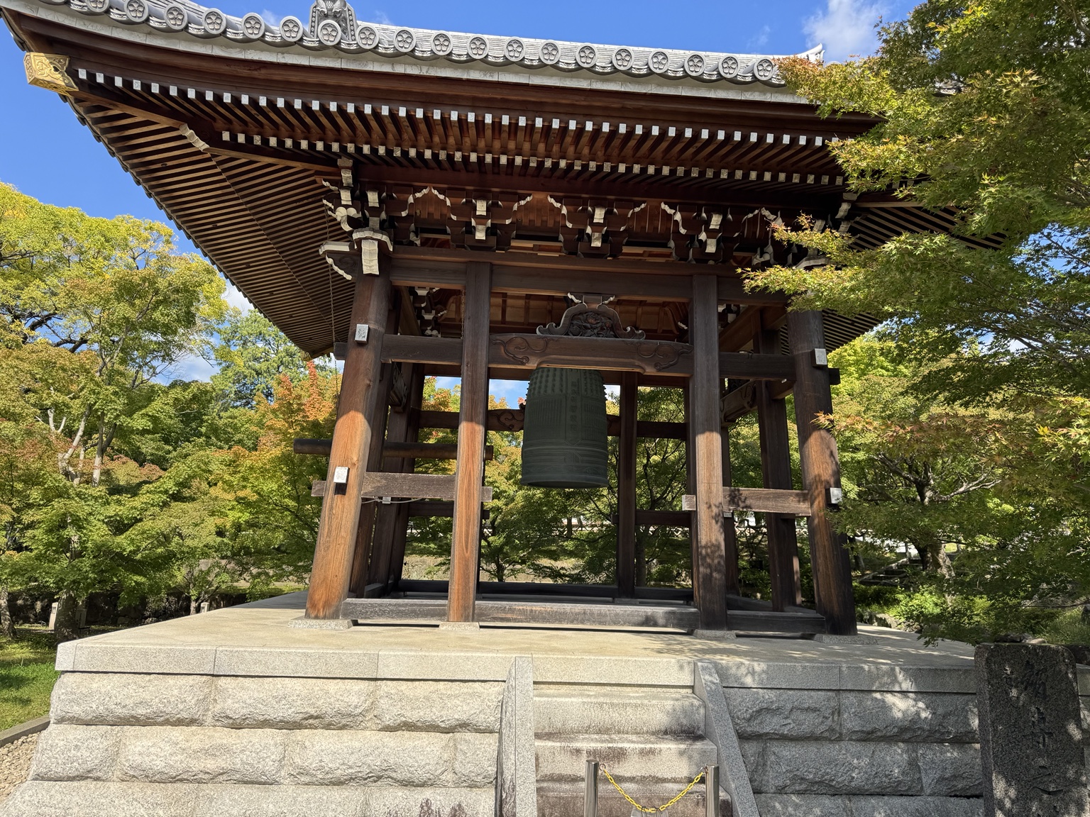 A wooden bell pavilion among green trees.