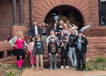 Students and staff in themed dress-up outfits posing together on the front steps of the Fitzroy Mansion