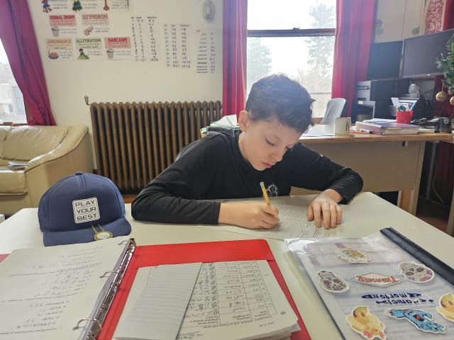 A student writing at a desk, surrounded by binders and worksheets