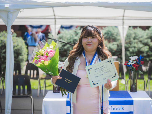 A graduate with her diploma, a bouquet, and an Excellence in Mathematics award