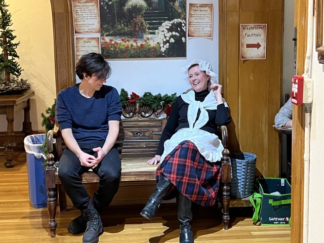 A guest in Victorian costume seated beside the Christmas tree