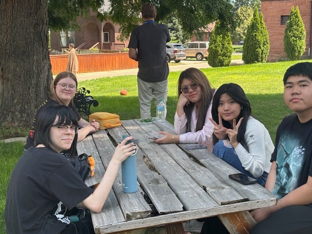 Students sitting together at a picnic table on the lawn outside the mansion