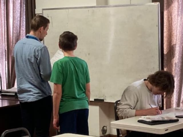 A teacher working through a problem at the whiteboard with a middle school student