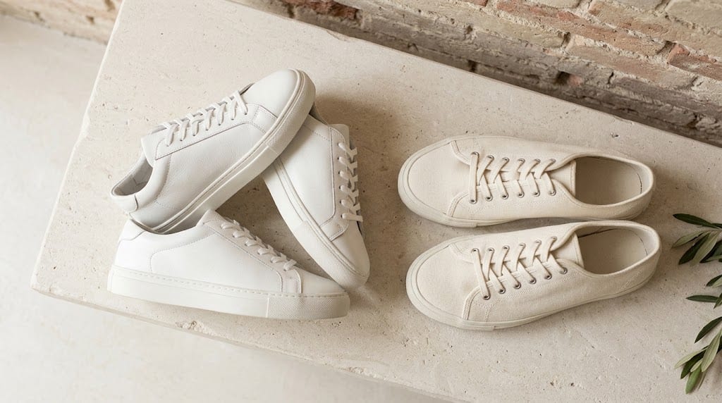 Un par de zapatillas minimalistas de cuero blanco apoyadas contra una pared de ladrillo visto