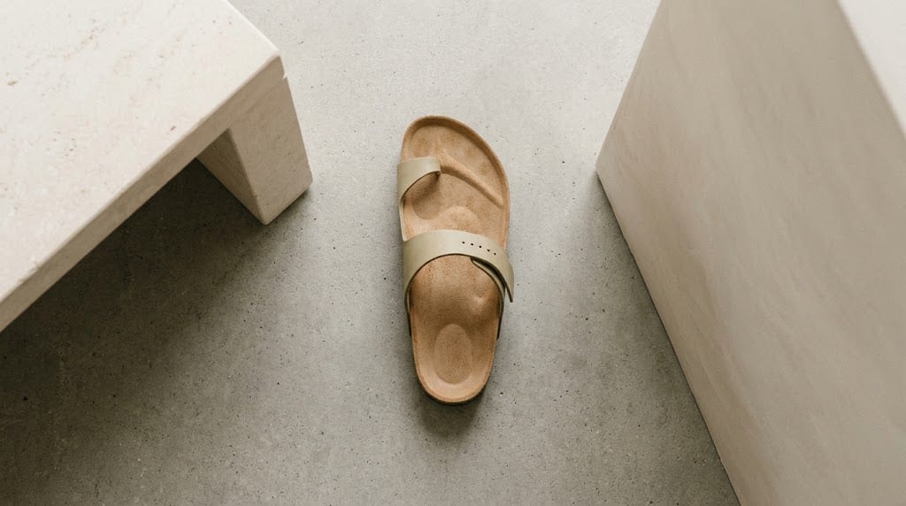 A molded cork footbed sandal sitting isolated on raw unpolished concrete, showing the distinct contours of the heel cup and the longitudinal