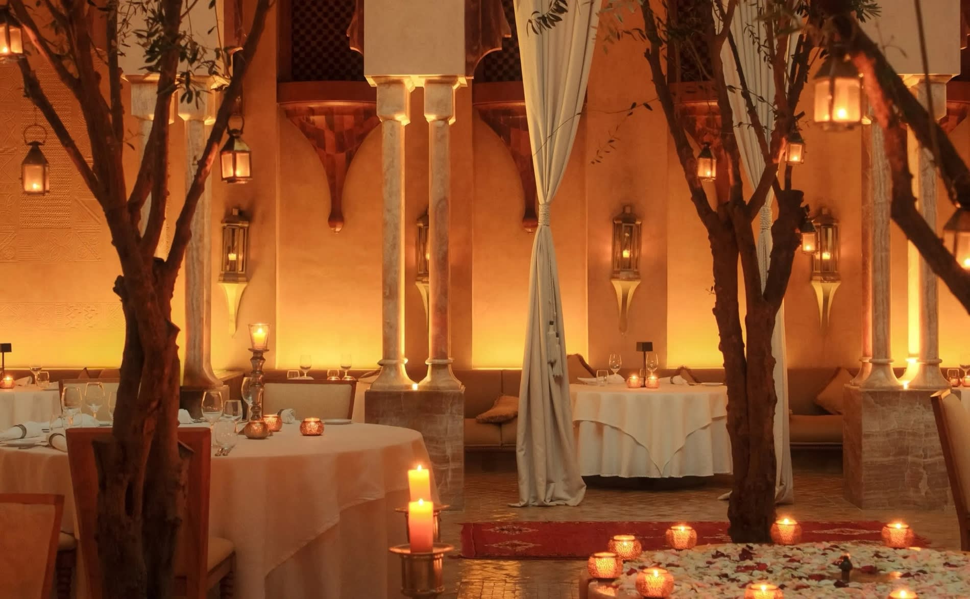 Patio du Moroccan Restaurant de l'Amanjena a Marrakech, tables dressees, oliviers et lanternes allumees le soir