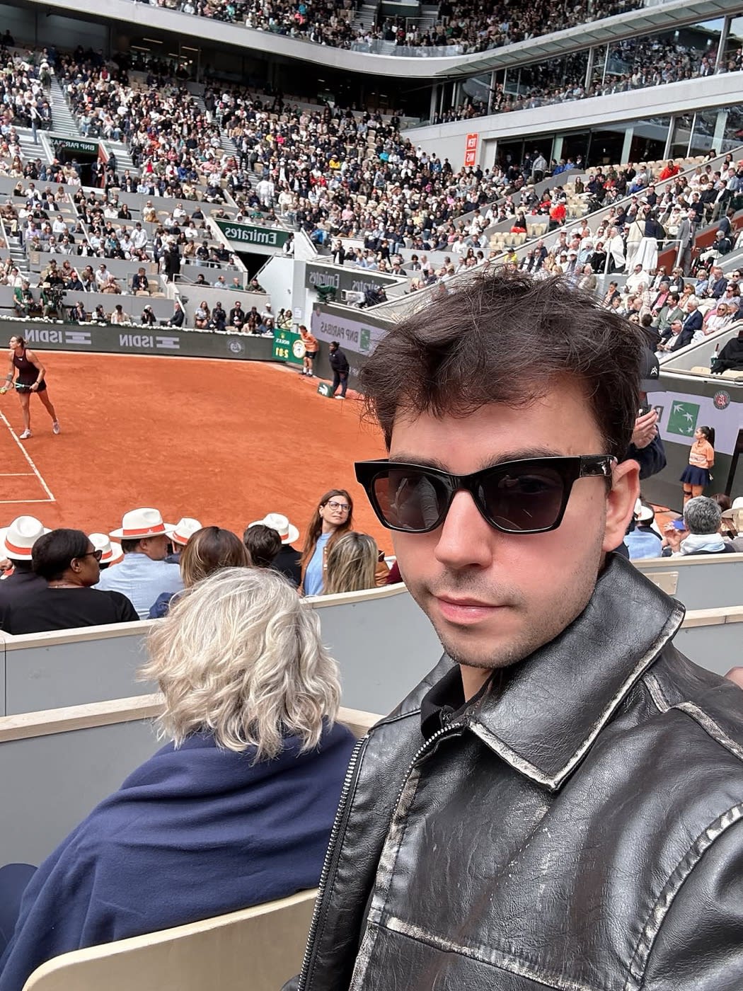 Raphaël Simon dans les tribunes de Roland-Garros, court en terre battue en arrière-plan