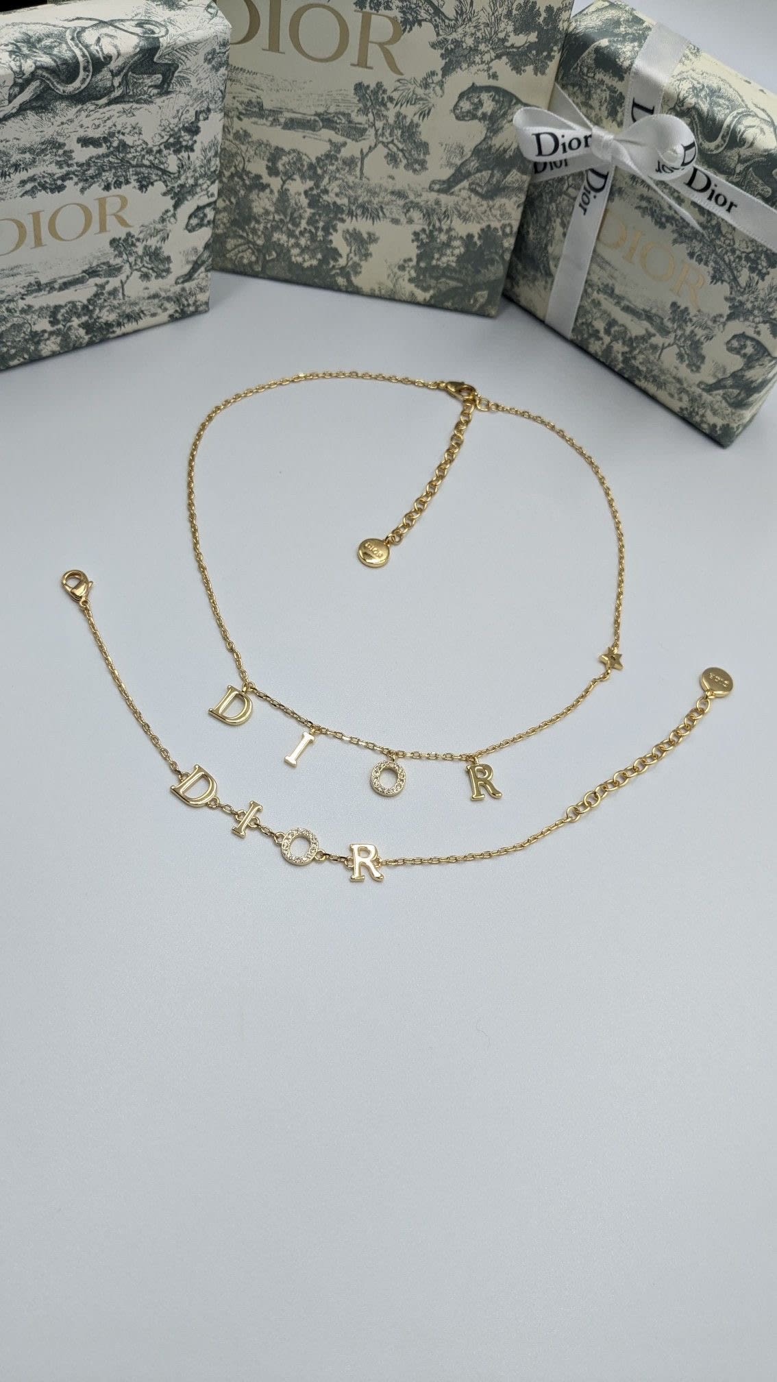 Gold Dior lettering necklace on a pale background with Dior packaging