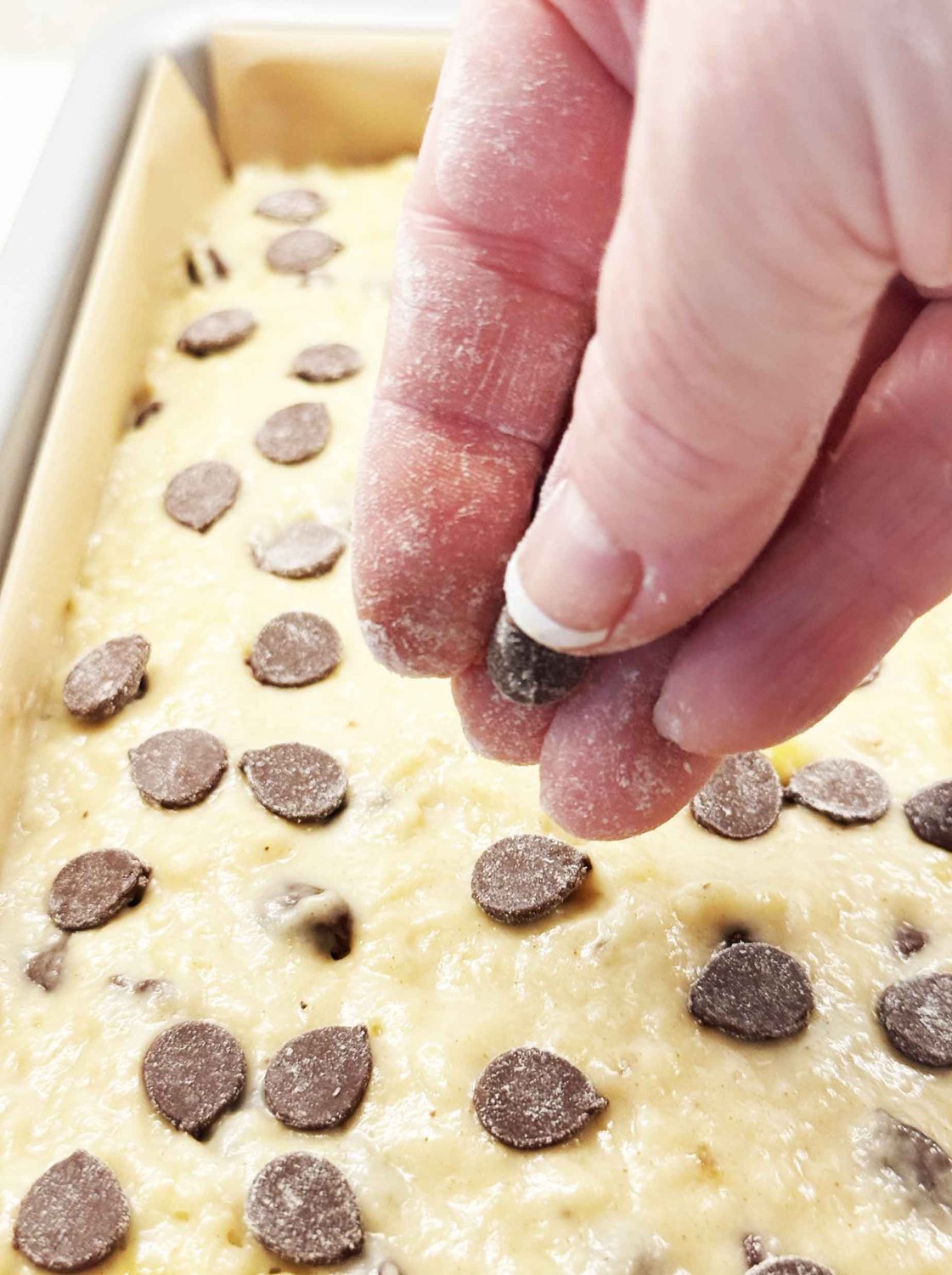 Reserved chocolate chips being sprinkled over the top of banana bread batter before baking