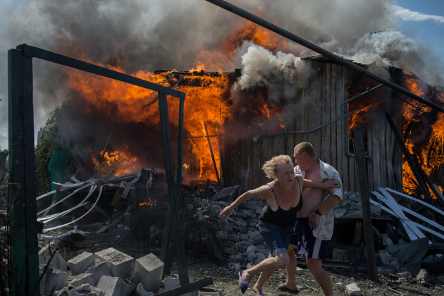 Photojournalism Single Image Winner. Civilians escape from a fire at a house destroyed by an air attack in Donbass, a village in Luhanskaya, eastern Ukraine, on 2 July 2014. Photo © Valery Melnikov.