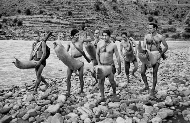 Kunar province, 1980. Armed mujahideen carry animal skins to use as inflatable buoys to cross rapids.