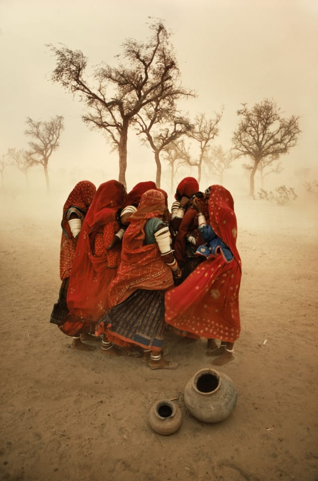 Dust storm, Rajasthan, India, 1983. McCurry once said, “You can’t get hungup on what you think your “real” destination is. The journey is just as important.” The evidence of his attitude was amply realized when he was driving along a highway in Rajasthan, India. He was stopped for a while by a dust storm and he captured the moment a group of workers were protecting each other from the choking dust. Copyright Steve McCurry.