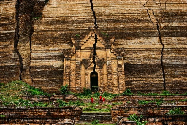 Mingun Pagoda, Mandalay, Burma 1994. Earthquakes caused these deep cracks to appear in the incredible Mingun Pagoda. Built to house a relic of the Buddha, the brick structure was originally intended to be over 150 metres tall. However, the technology was not capable of enabling its full construction and so it reaches 30 metres. Three monks are seen climbing the steps. Copyright Steve McCurry.