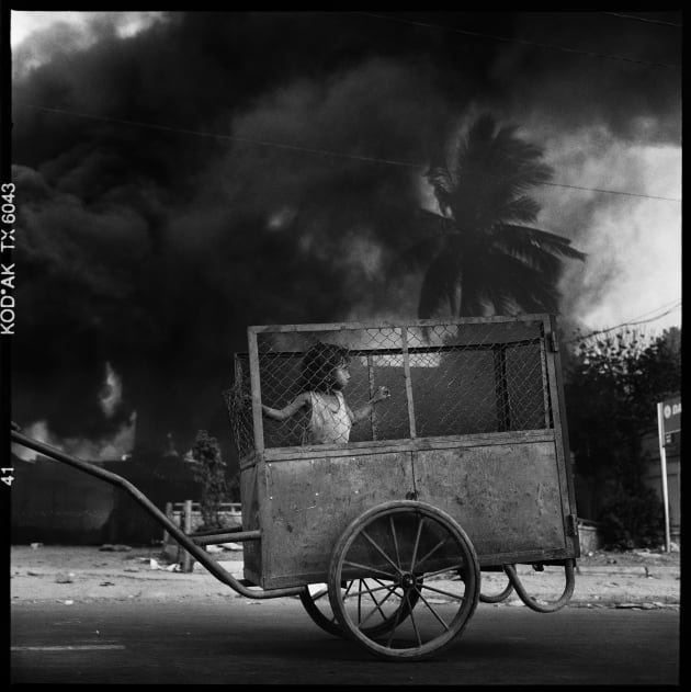 A child is pushed in a cart along the main coastal promenade in Dili as parts of the city go up in flames following the violence and chaos of post referendum for Independence from Indonesia. East Timor, 1999.