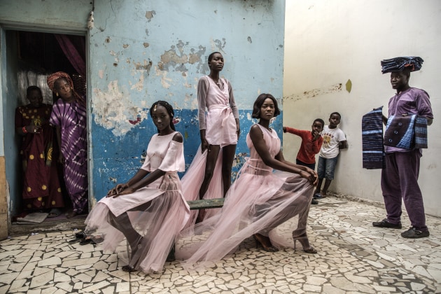 Diarra Ndiaye, Ndeye Fatou Mbaye and Mariza Sakho model outfits by designer Adama Paris, in the Medina neighborhood of the Senegalese capital, Dakar, as curious residents look on. © Finbarr O'Reilly