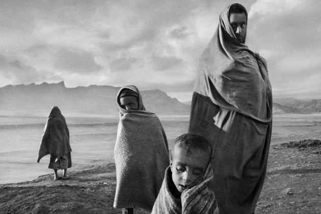 Draped in blankets to keep out the cold morning wind, refugees wait outside Korem camp. Ethiopia, 1984. © Sebastião Salgado