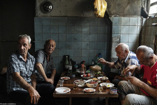 Politics of Food, Sandro Maddalena. Italy, 'Old friends'. Tskaltubo - Refugees from the Abkhazian - Georgian conflict gather in the basement of an abandoned sanatorium to share their food. Almost thirty years after the conflict, Abkhazian refugees are still living in abandoned buildings in conditions of poverty.