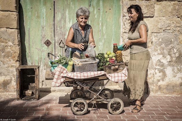 Winterbotham Darby Food for Sale, Joseph P Smith, Malta, 'Street Vendor'. A lady sells capers and other delicacies from her old pram on the streets of Marsaxlokk, a fishing village in Malta.