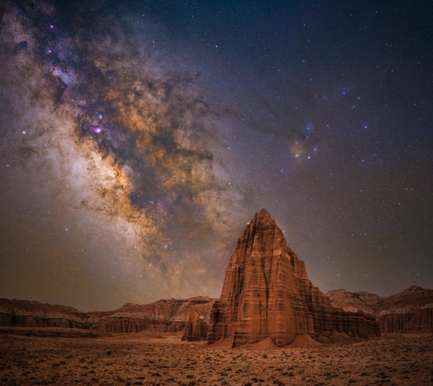 © Bryony Richards - “Temple of the sun” 
Capitol Reef National Park, Utah – USA
The Milky Way core rises before dawn under the southern skies of Capitol Reef National Park’s “Temple of the Sun.” This area of the Colorado Plateau Desert, known for its domes, hoodoos, fins, reefs, natural bridges, and slot canyons, includes the Temples of the Sun and Moon.
These Jurassic-aged sandstone monoliths, which formed as sandy mud on a tidal flat, tower above the otherwise flat desert floor. It seems like more than a coincidence that the Temples line-up perfectly with the Milky Way, their vibrant orange colors seemingly reflecting the color of the stars above.