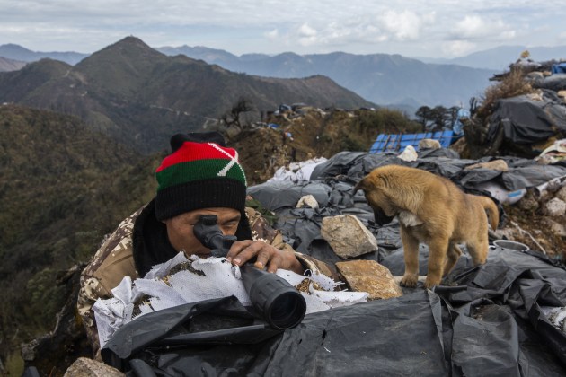 © Hkun Lat, Highly Commended, 2019. A KIA soldier looking over the Myanmar military post through a scope at Zion frontline at border pillar 6, between China and Myanmar. The opposite posts between KIA and Myanmar military are only far part less than 20 meters. However, after 2013, they only observe each other from their positions on top of the mountains. Kachin State, 2018. From the series, The Peace House.