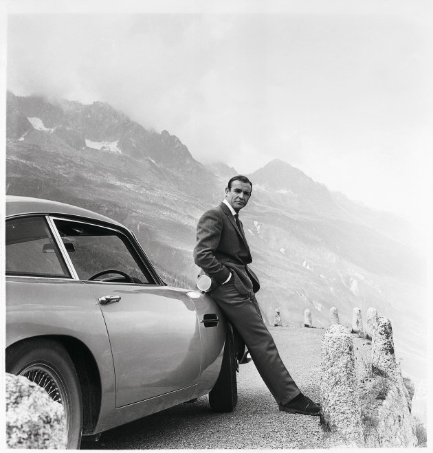 Goldfinger (1964). James Bond (Sean Connery) and his iconic Aston Martin DB5 which first appeared on screen in Goldfinger. Photograph by Bert Cann. Image supplied by Leica. (GOLDFINGER © 1964 Danjaq, LLC and Metro-Goldwyn-Mayer Studios Inc. All Rights Reserved.)