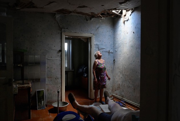 © Kate Geraghty. Winner, Feature/Photographic Essay. Invasion of Ukraine - Civilian Impact. Living on the frontline: Zoya Shaposhnik, 67, looks up at the hole in her ceiling from a missile strike. Her disabled husband narrowly escaped injury or death in their home in Krasnohorivka. Zoya Shaposhnik did not evacuate as many others have in the town, instead staying to care for her husband. Their roof and other parts of their home have been destroyed. Krasnohorivka, Donetsk Oblast, Ukraine. June 16, 2022.