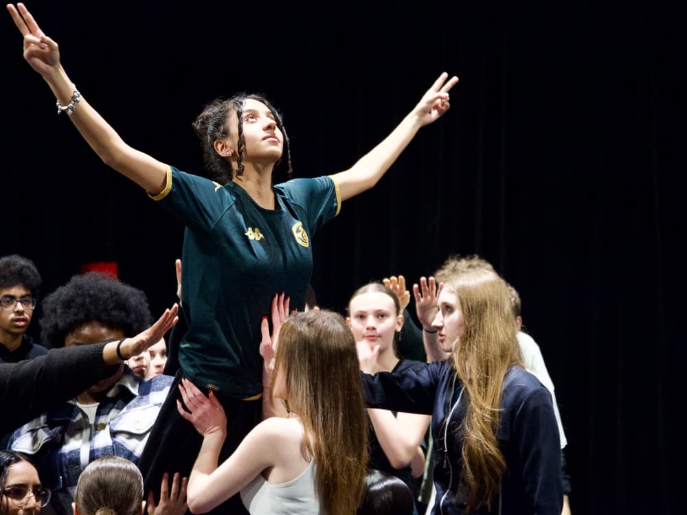 A young woman celebrates as she is lifted into the air by a group of people, symbolizing victory.