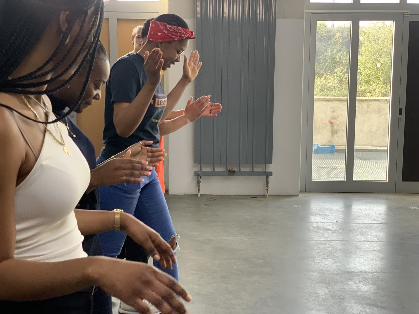 A group of young women in a room, raising their hands and clapping together, participating in a rhythm game.