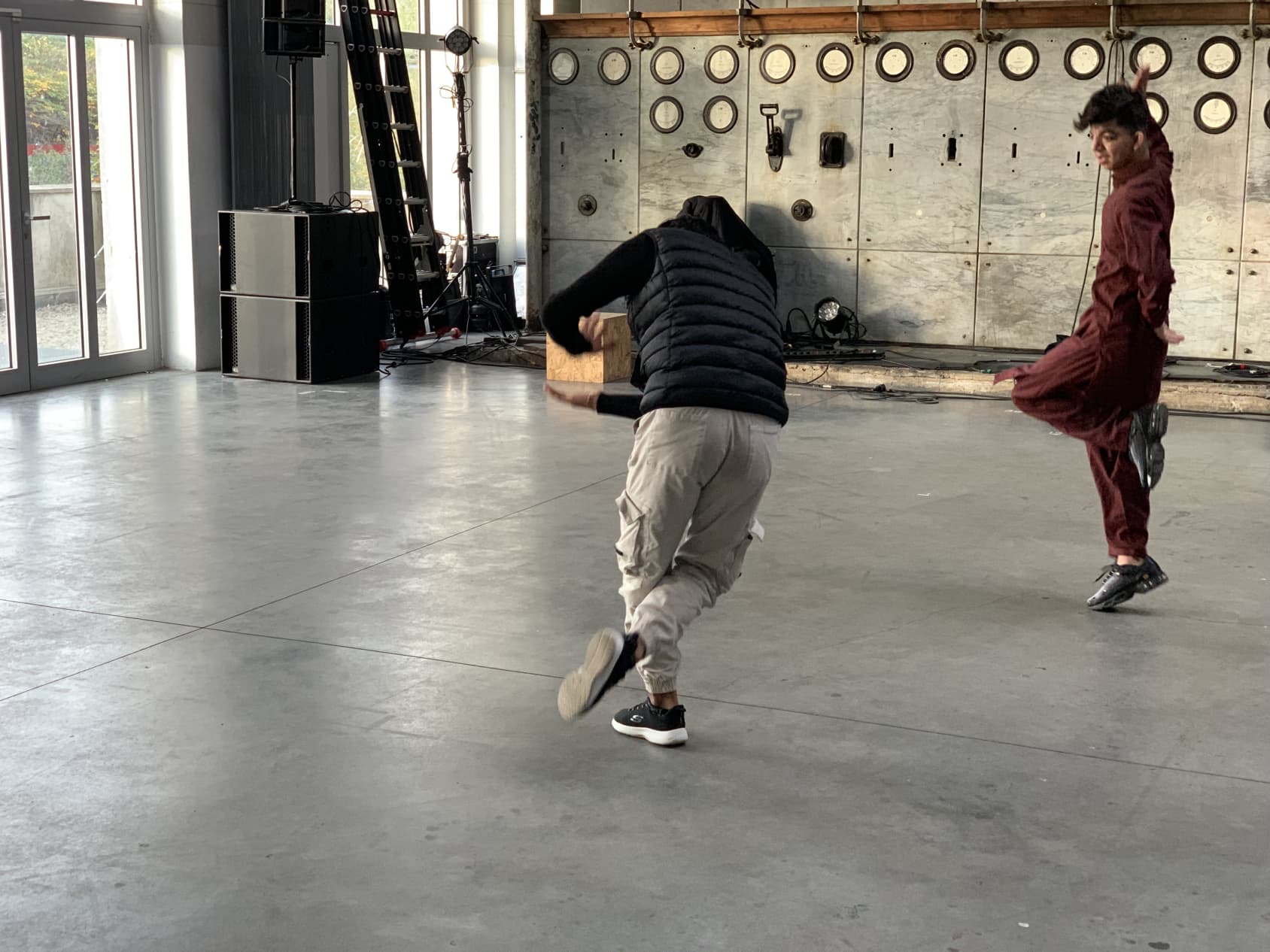 Two people dancing together in an empty room, performing a traditional Afghani dance.