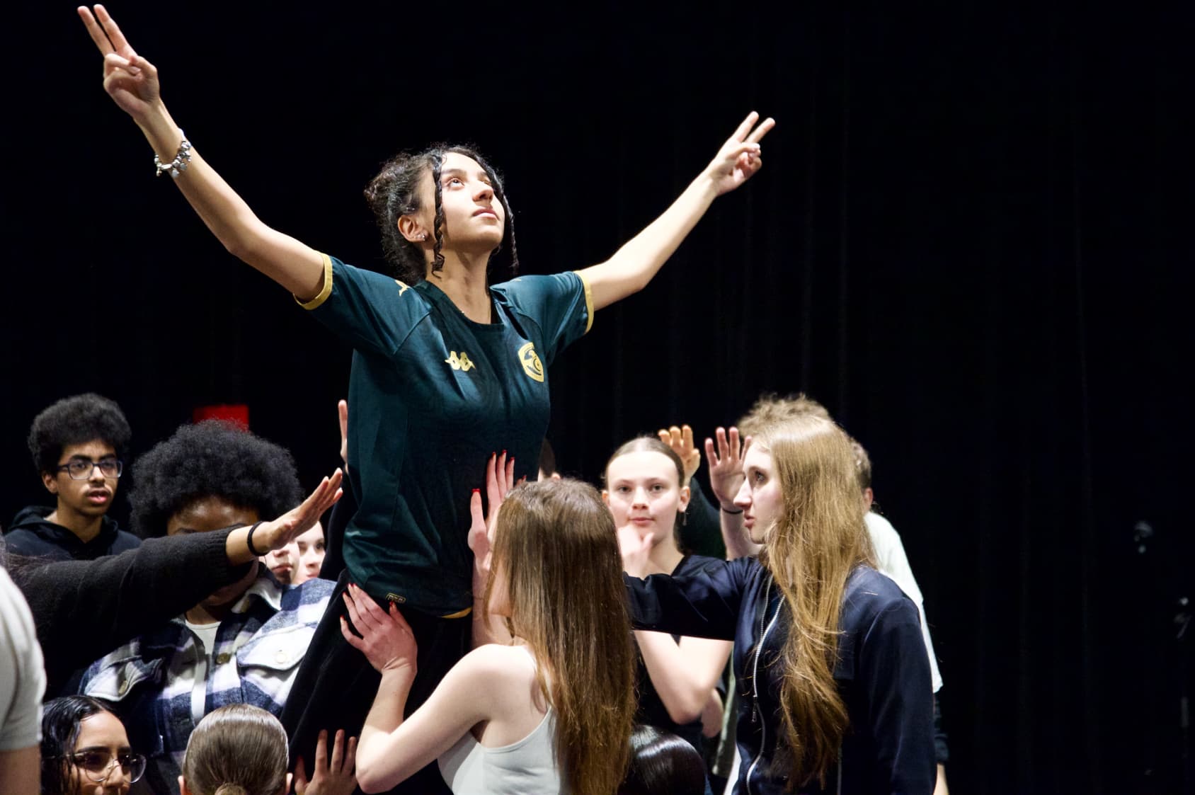 A young woman celebrates as she is lifted into the air by a group of people, symbolizing victory.