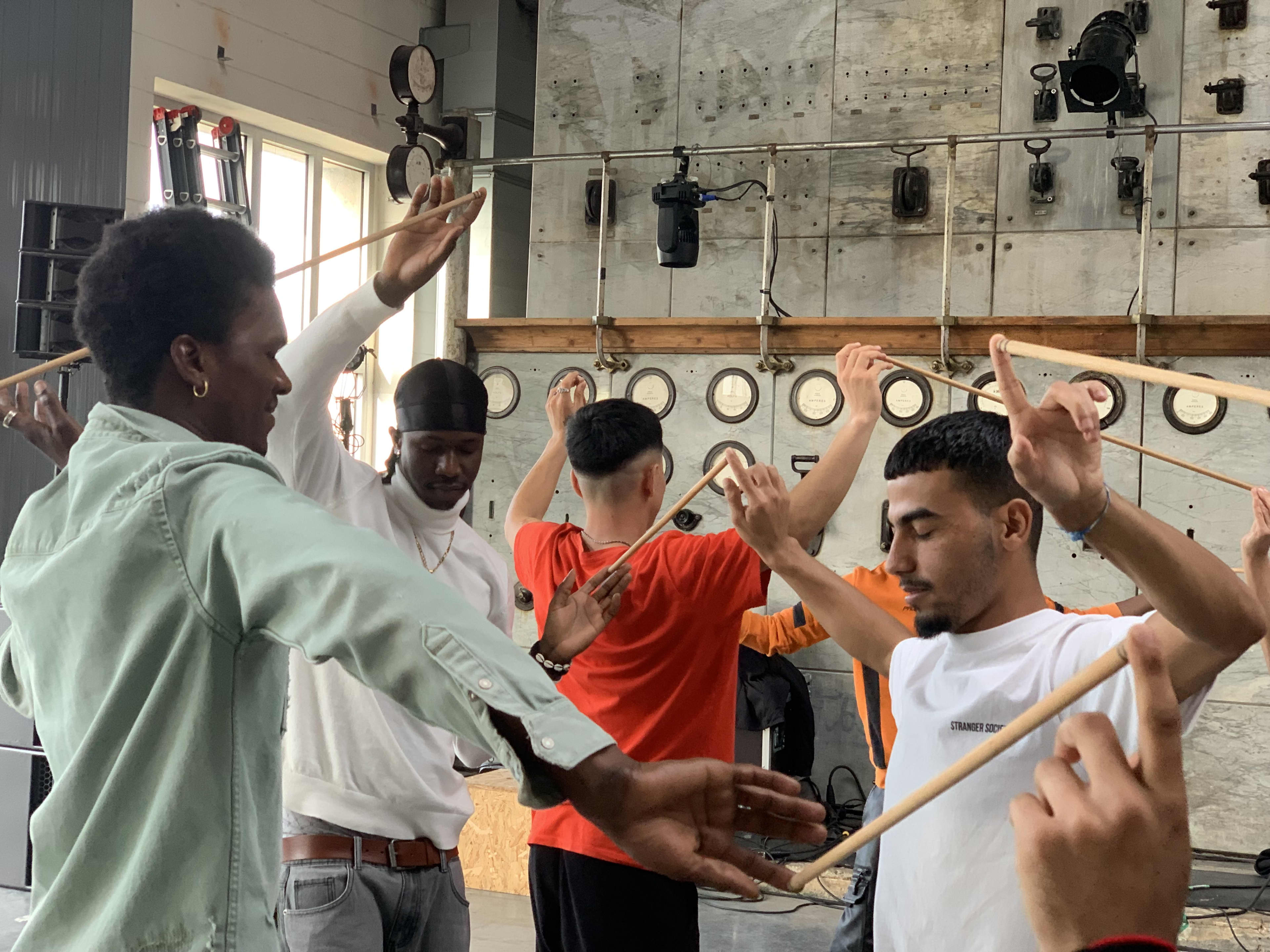 A group of young people, eyes closed, collaborates on a game-like task by holding sticks pressed between their hands.