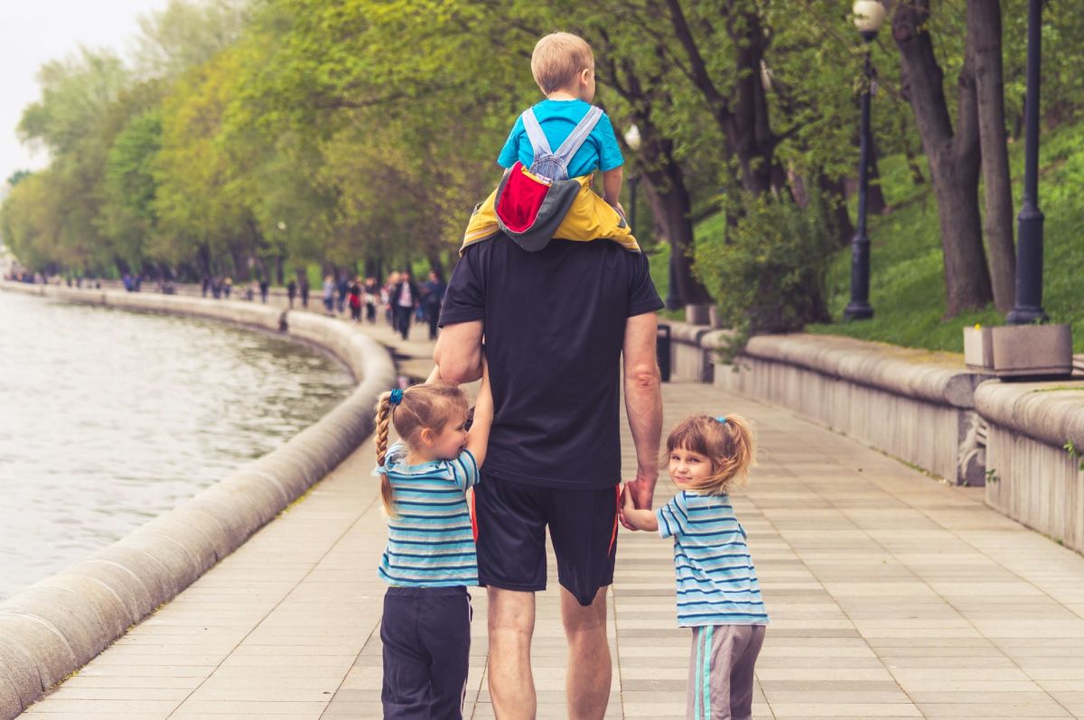 Padre paseando con sus tres hijos pequeños junto a un lago