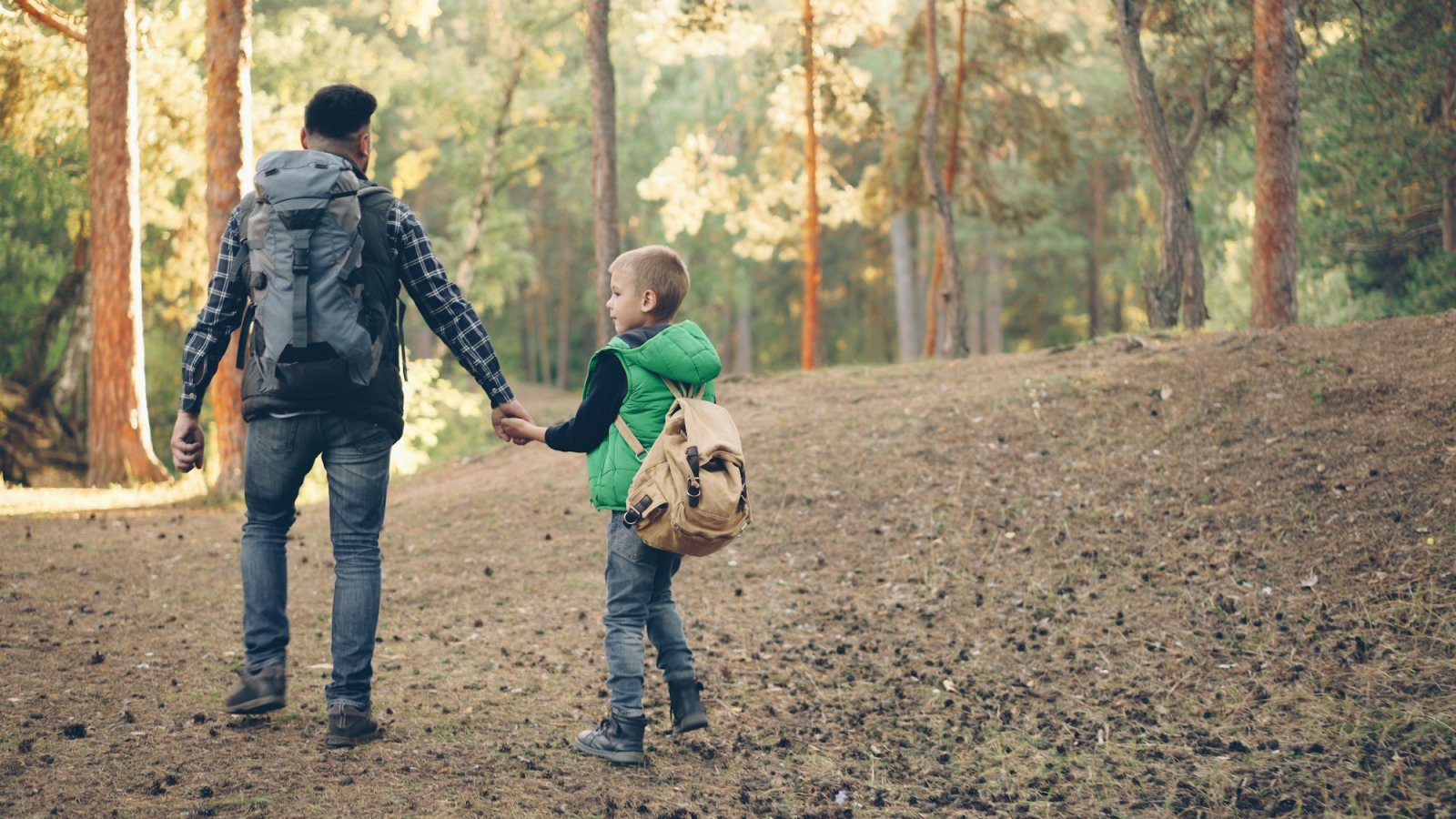 Padre e hijo caminando juntos por un sendero de bosque con mochilas
