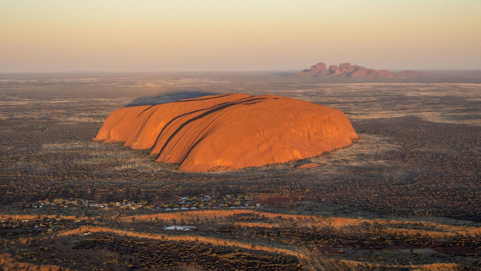 Vista aérea de Uluru al atardecer con Kata Tjuta al fondo, desierto rojo del centro de Australia
