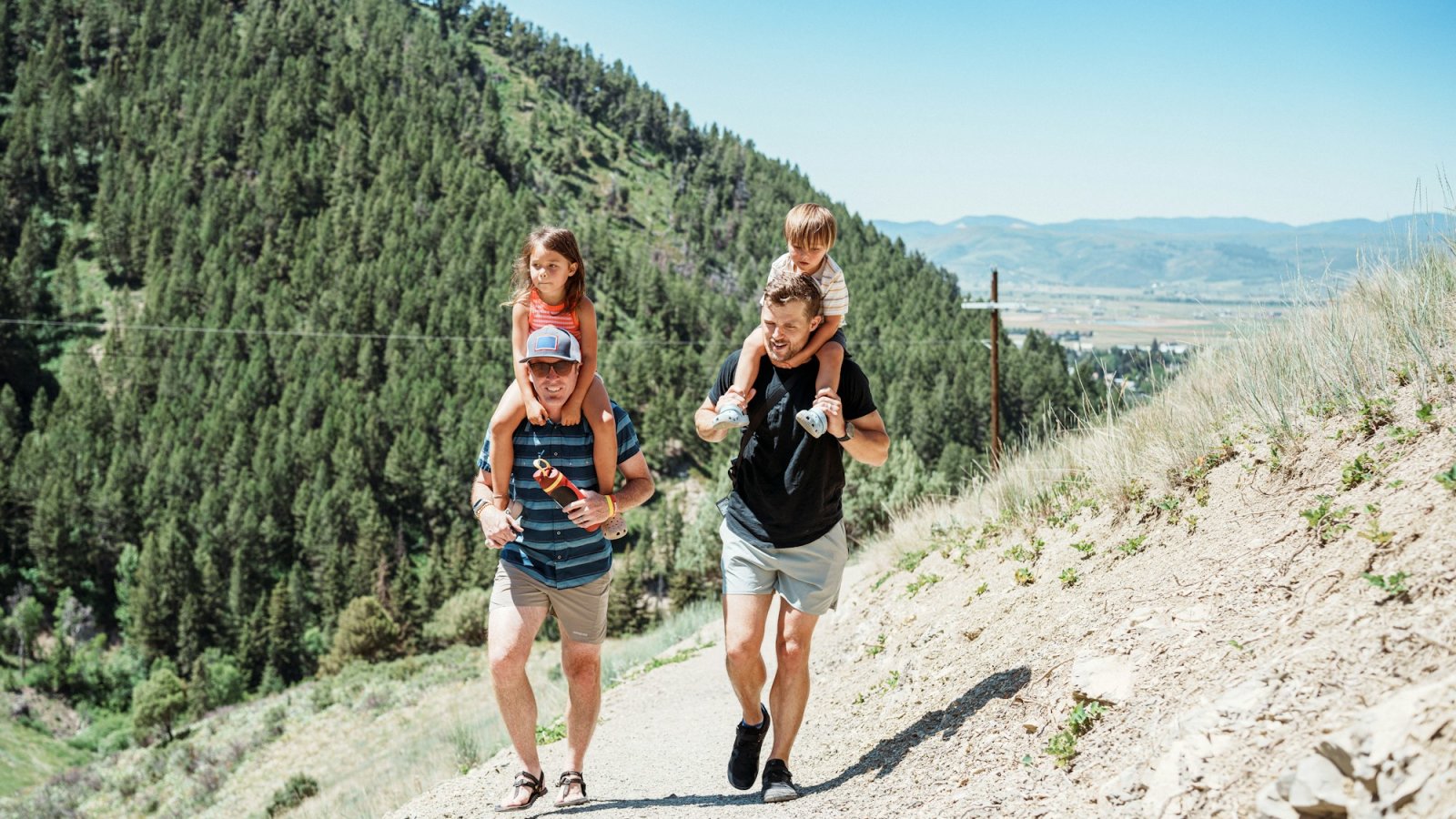 Padres llevando a hombros a sus hijos pequeños por un sendero de montaña