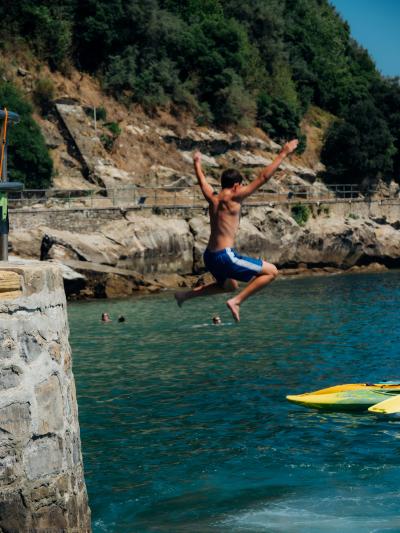 Adolescente saltando al mar desde un muelle de piedra